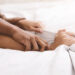 Passion in bed. African-american couple hands pulling white sheets in ecstasy, closeup
